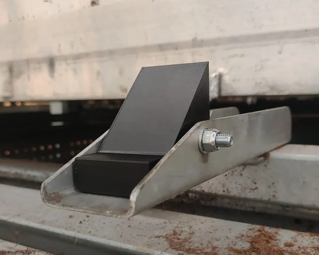 een close-up van een metalen steun met een zwarte weerhaak en een bout met moer.