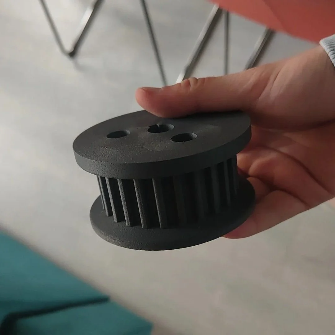 Een hand die een 3D geprint grijs kunststof tandwiel vasthoudt.