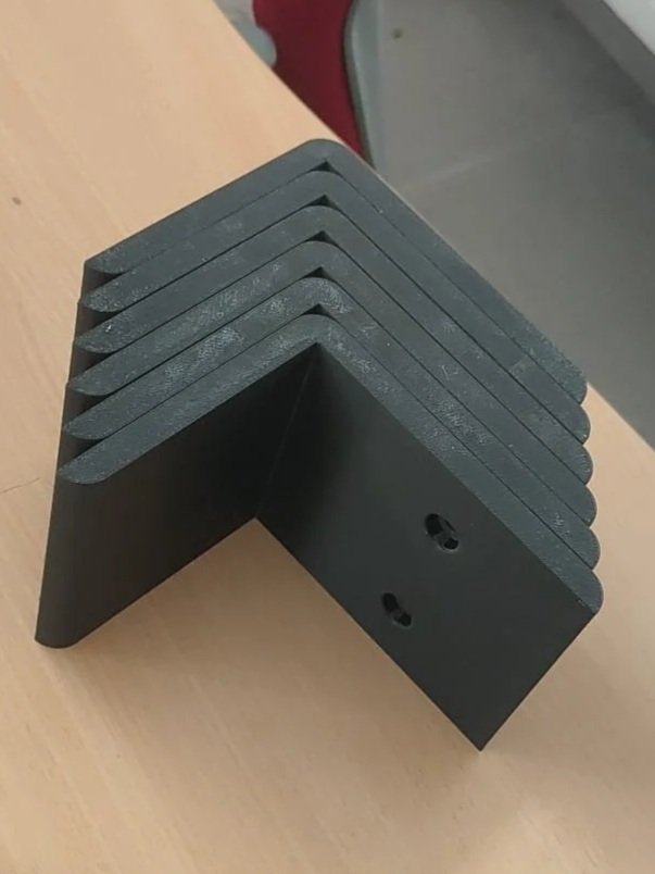 Zes zwarte L-vormige metalen hoekstukken gestapeld op een houten tafel.