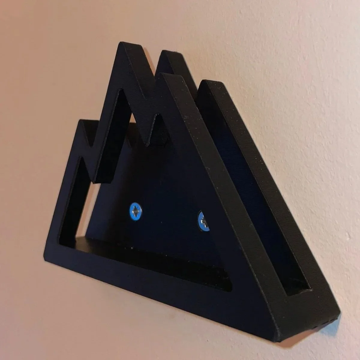 Een zwarte, driehoekige kunststof muurbeugel gemaakt voor een snowboard met twee schroeven op een lichte muur.