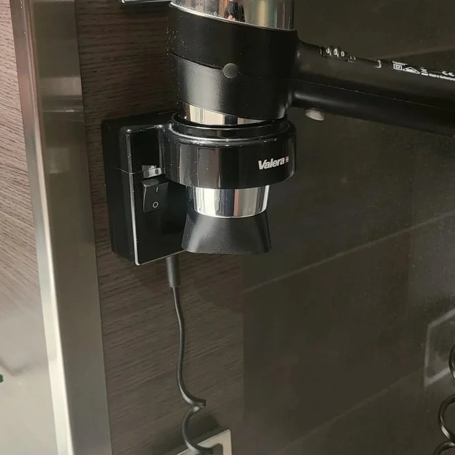 Een close-up van een elektrische föhn met 3D geprint mondstuk een zwart en zilverkleurig ontwerp, aangesloten op een stopcontact.