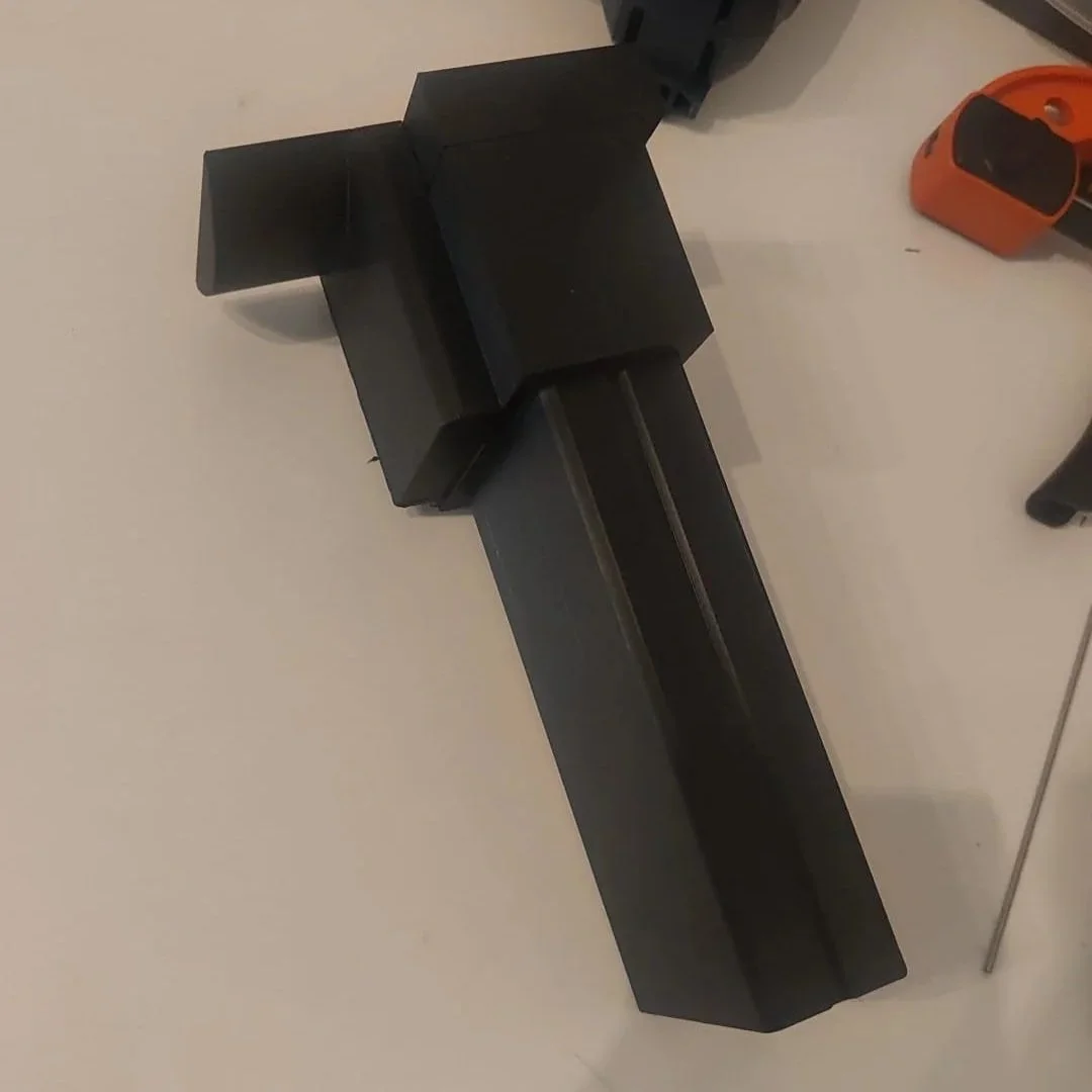 Een zwart L-vormig steun op een witte tafel, met gereedschap op de achtergrond.