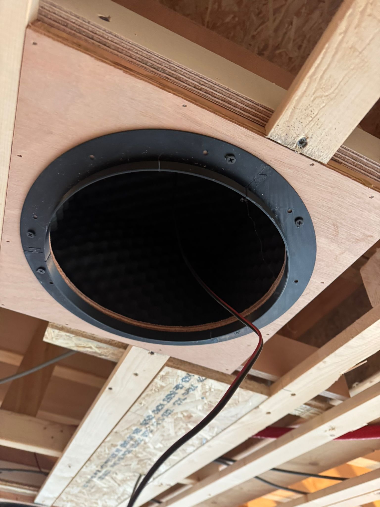 3D geprinte installatie van een luidspreker in een houten plafond, met een rode en zwarte draad eraan.