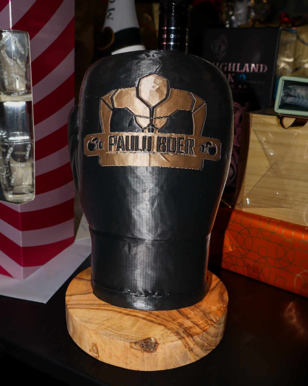 Een 3D geprinte zwarte bokshandschoen op een houten blad met het logo van private gym Paulo Boer