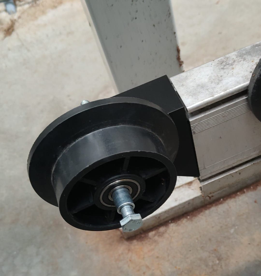 Een close-up van een rond, zwart kunststof wiel met een metalen as, bevestigd aan een metalen machine of constructie.