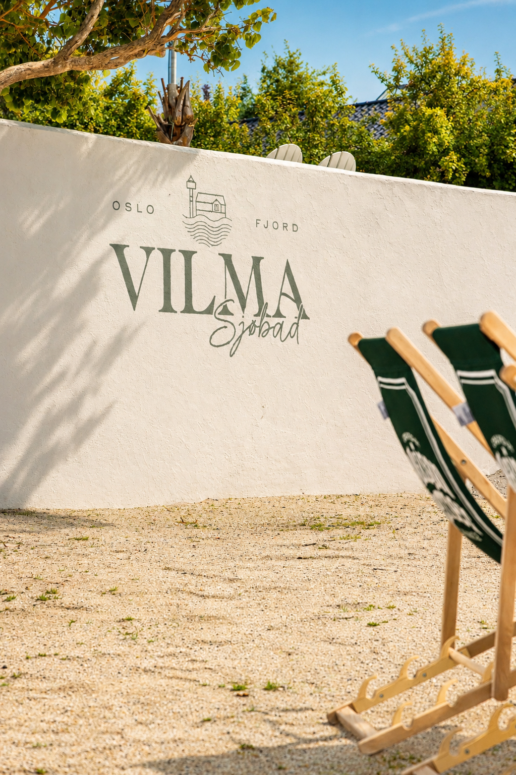 En mur med logoen til Vilma Sjøbad, i forgrunnen er det en strand med to strandstoler.