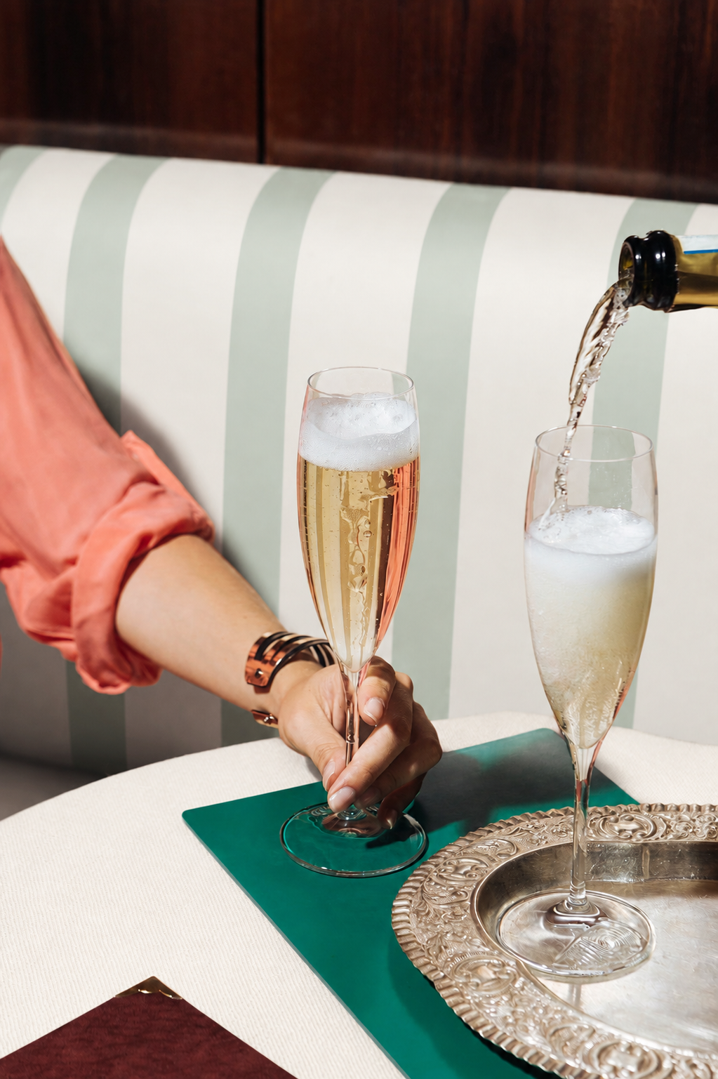 En hånd som holder et champagneglass  ved siden av et annet glass som blir skjenket