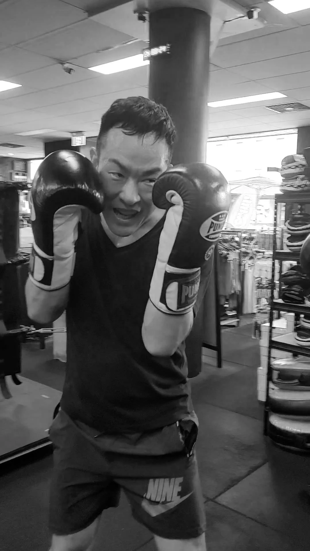 A man wearing boxing gloves and athletic clothing posing as if ready to box inside a store.