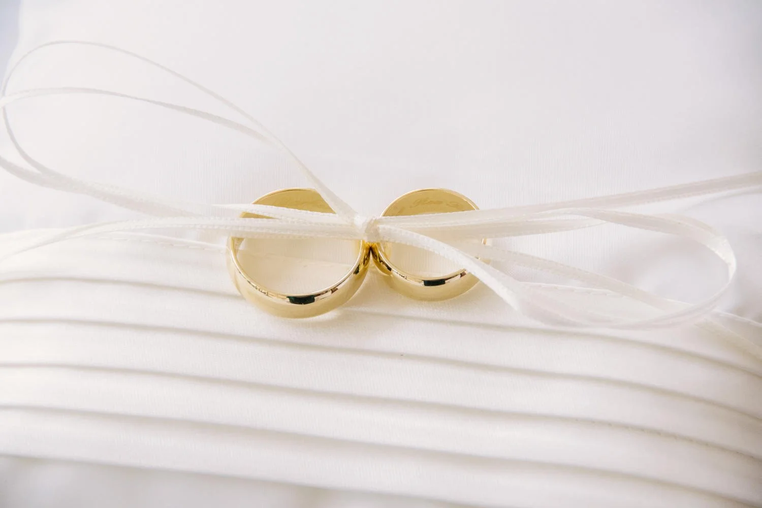 Zwei goldene Eheringe auf einem weißen Kissen, mit weißen Bändern gebunden.