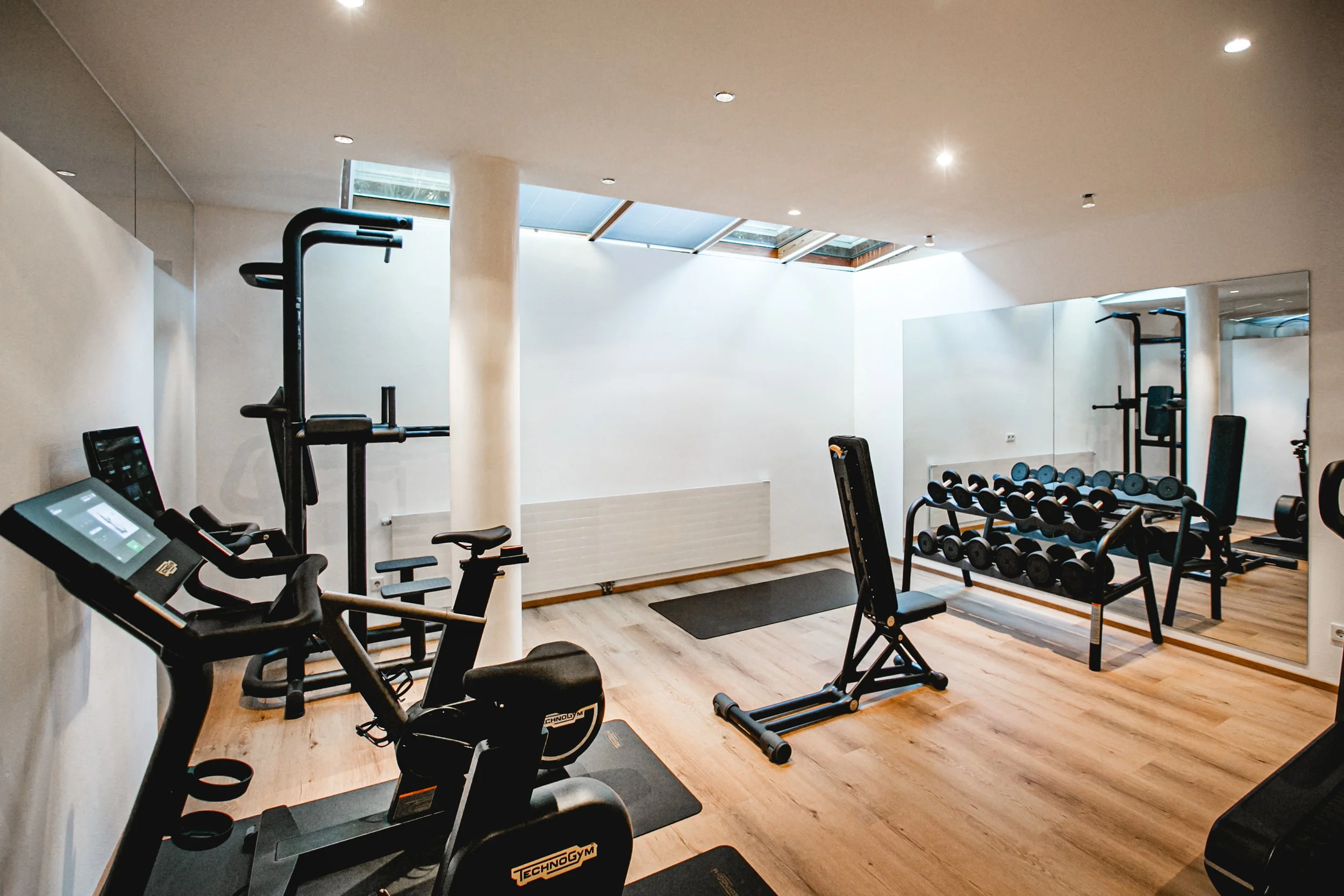 Modernes Fitnessstudio mit Geräten wie Laufband, Hanteln und Fahrradergometer.
