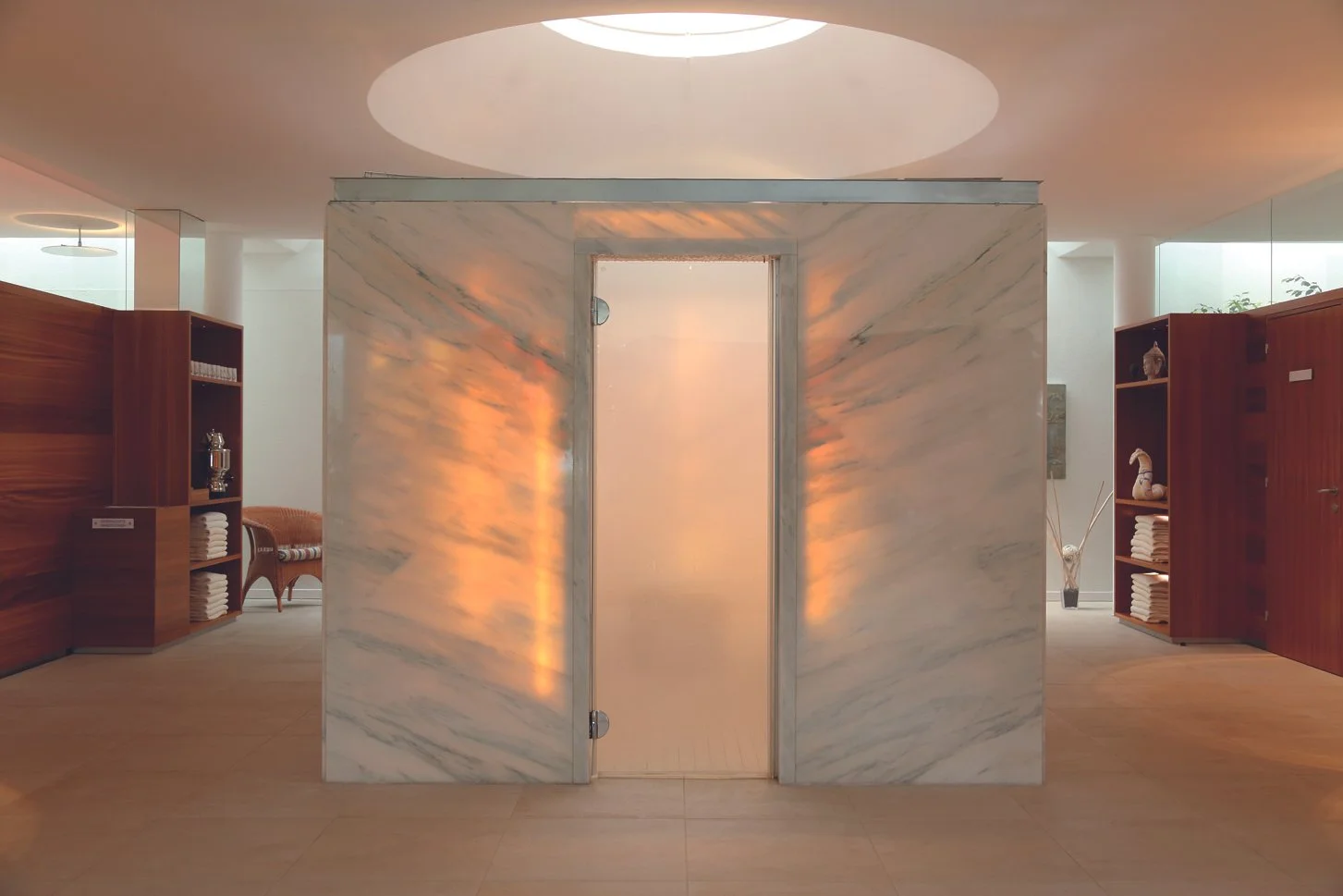 Innenraum eines modernen Bads mit Marmordampfbad und Holzregalen, die Handtücher und Dekorationen enthalten.