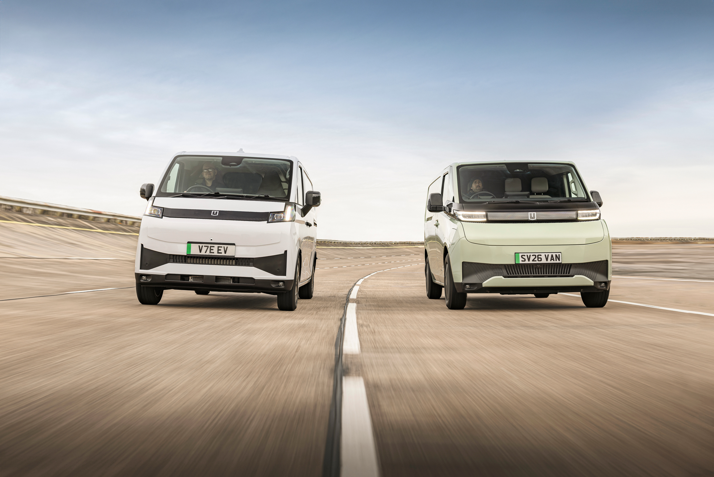 Two modern electric vehicles driving side by side on a track, with a clear sky above.