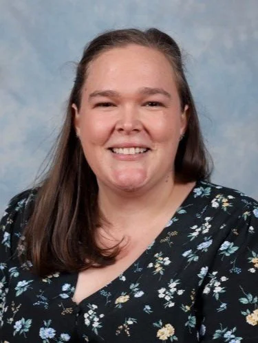 Woman smiling against a light blue background, wearing a floral-patterned top.