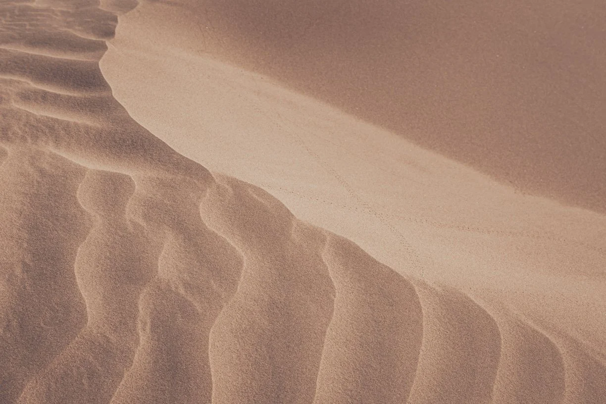 Close-up view of sand dunes with rippled patterns and smooth curves in desert landscape.