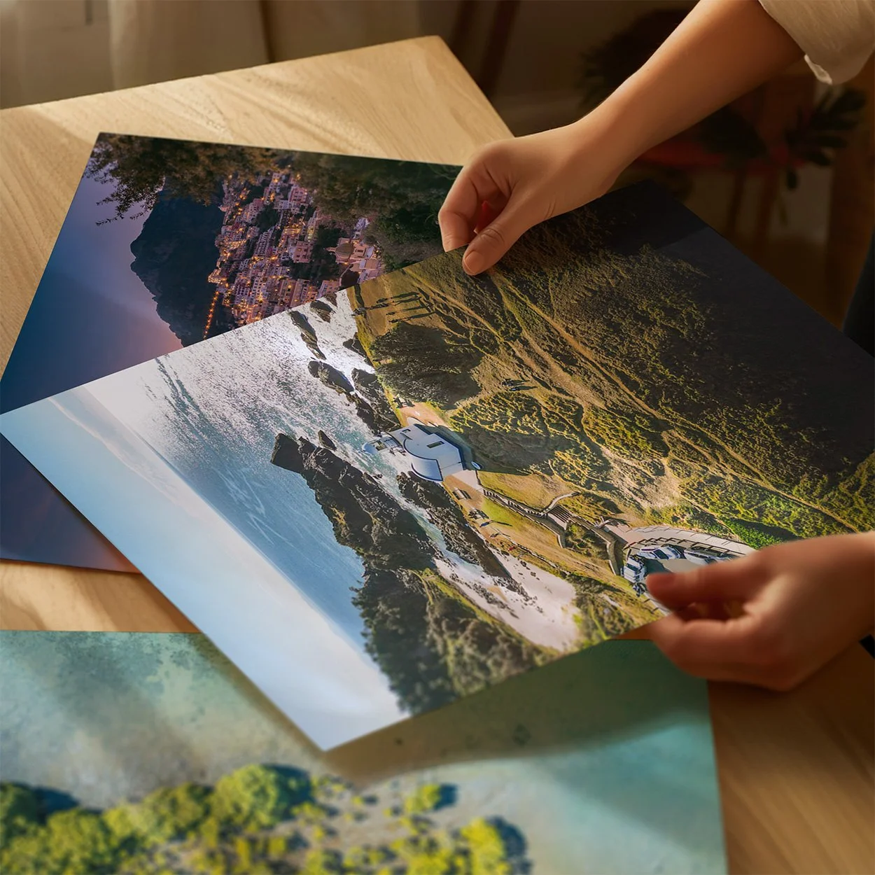Person flipping through large landscape photographs on a wooden surface.