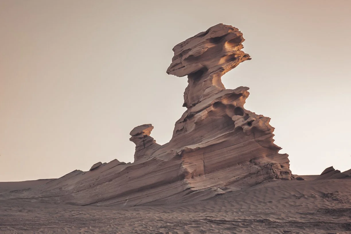 Unique desert rock formation with layered sandstone in a sandy landscape during sunset.