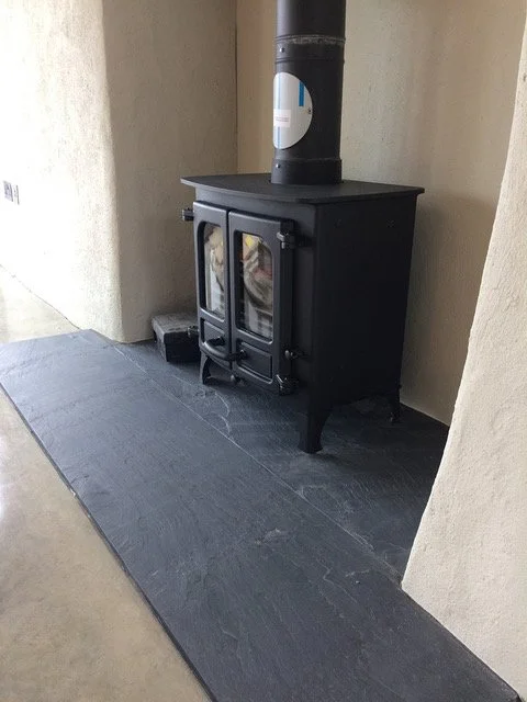 A black wood stove with glass doors on a Welsh slate hearth.