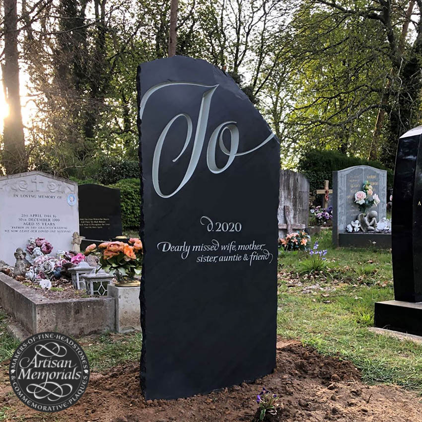 Black tombstone with a large white cursive "O" and inscription reading "D. 2020. Dearly missed wife, mother, sister, aunt, and friend."