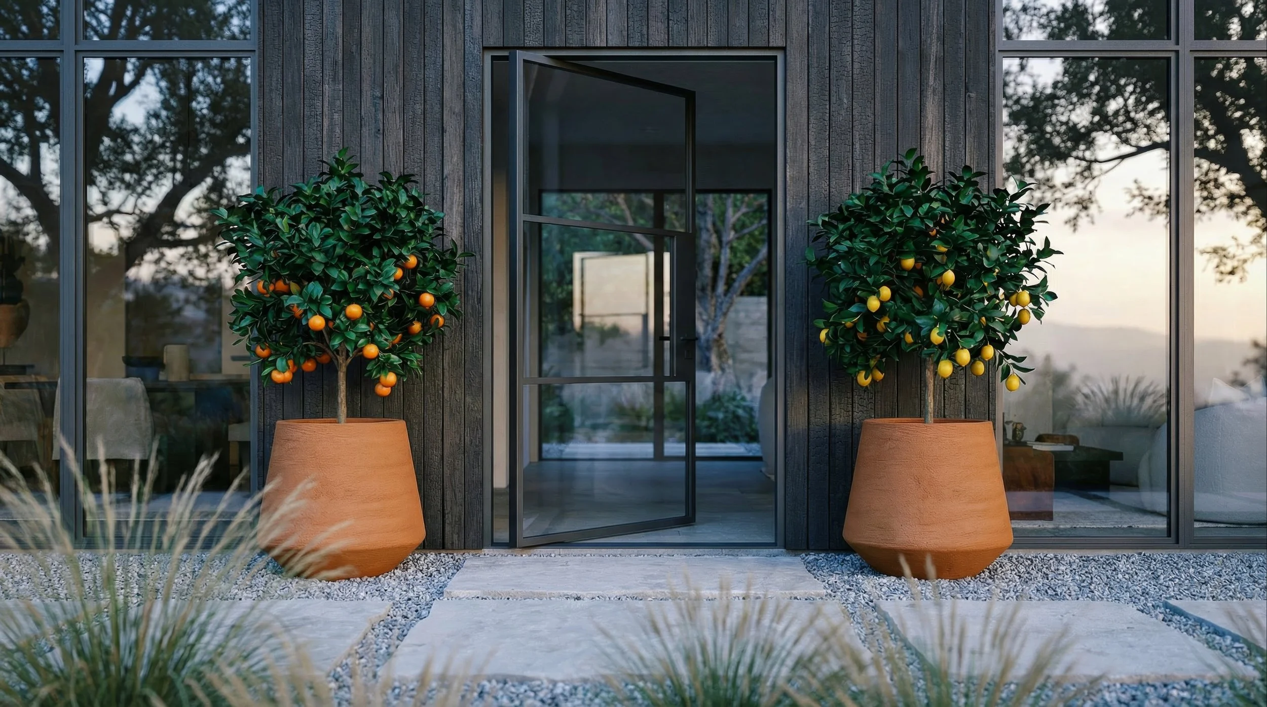 Two potted orange trees with green leaves and ripe oranges placed outside a modern glass door with a dark wooden wall background.