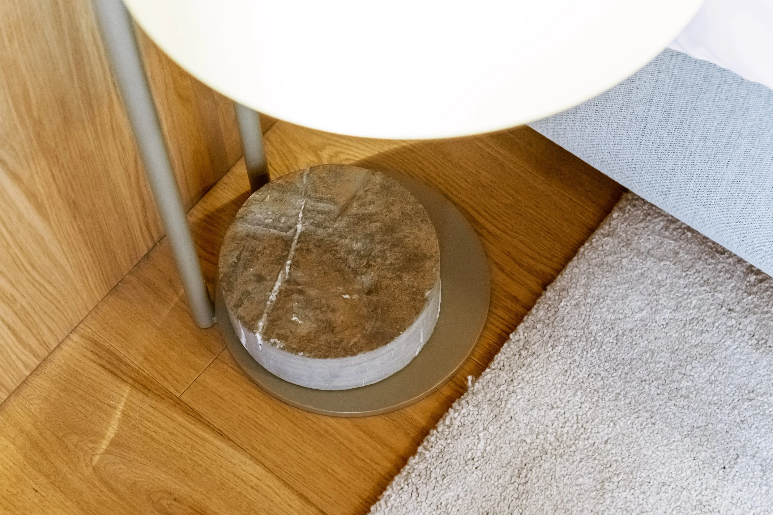 Close-up of a lamp with a stone base, sitting on a wooden floor next to a gray sofa and a beige carpet.