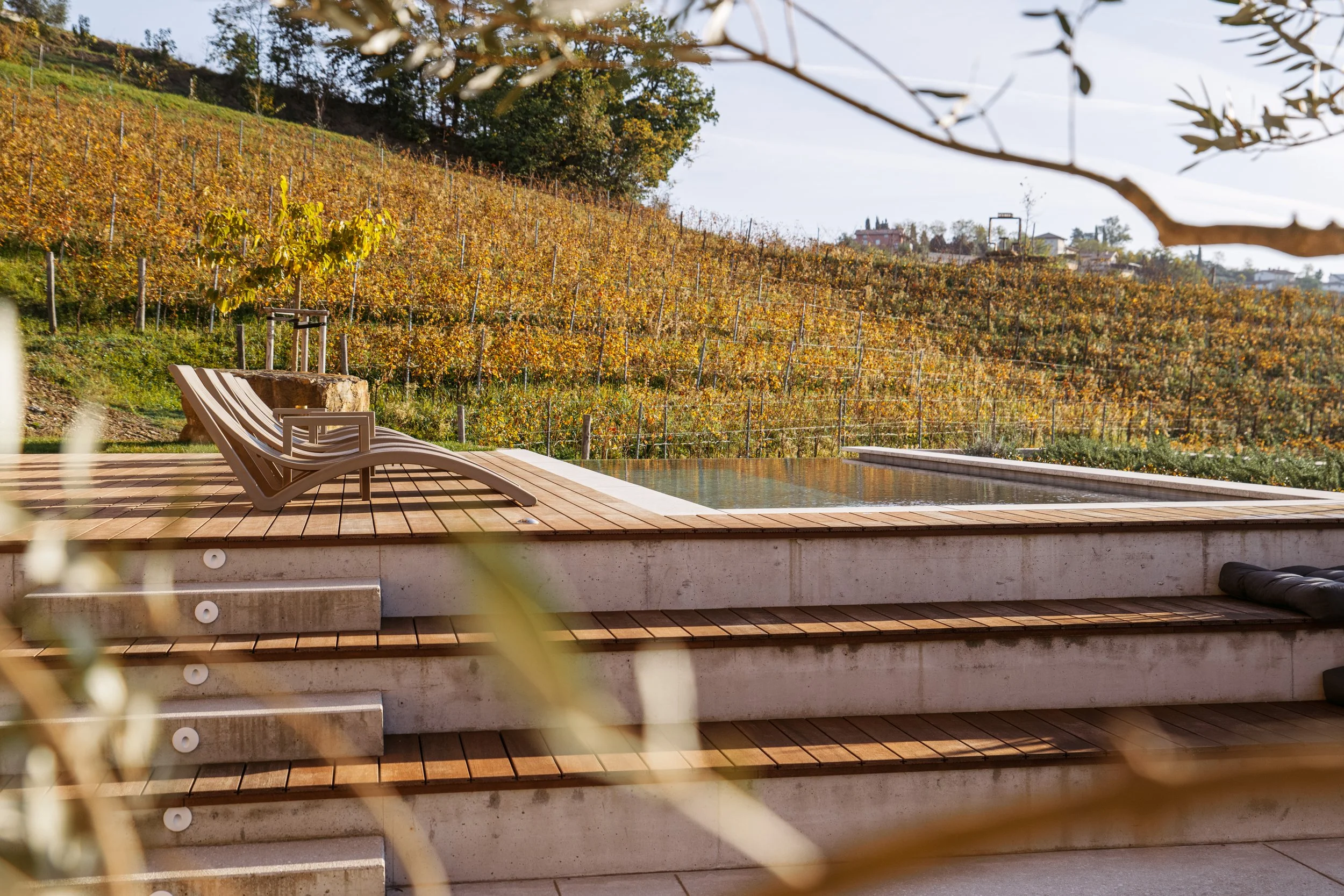 A wooden deck with two lounge chairs and a small pool, overlooking a vineyard on a hillside.