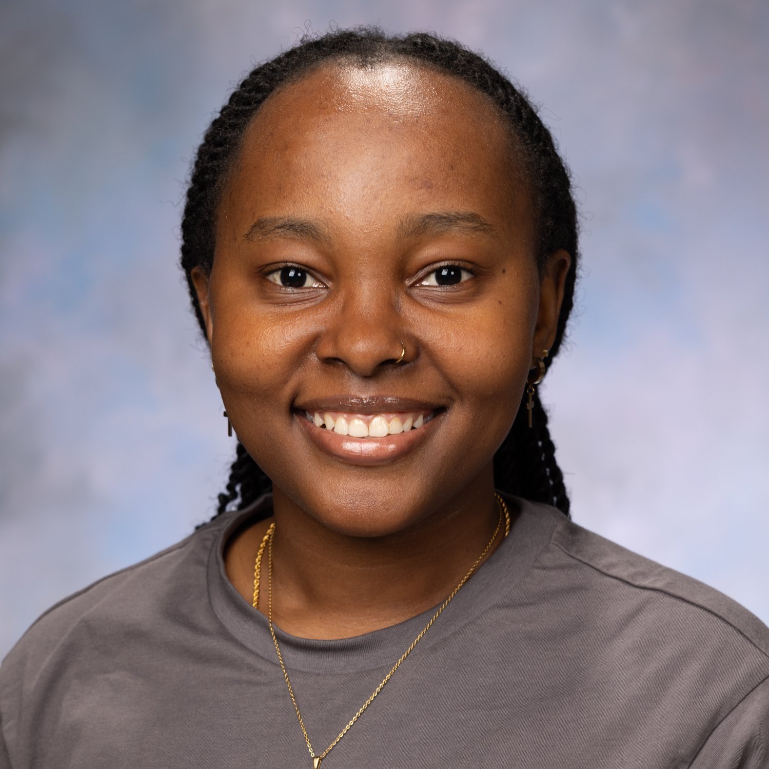Portrait of a smiling person wearing a gray shirt and a gold necklace, with a light blue and gray background.