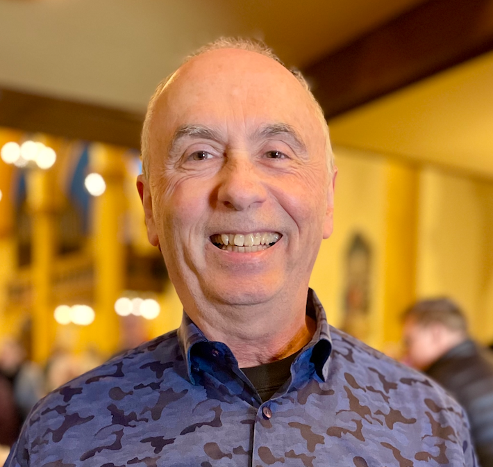 Stained glass window with floral patterns, featuring diamond shapes in various colors including white, purple, orange, and blue, set in an ornate frame.