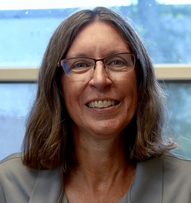 Smiling person in a blue shirt with gray background.