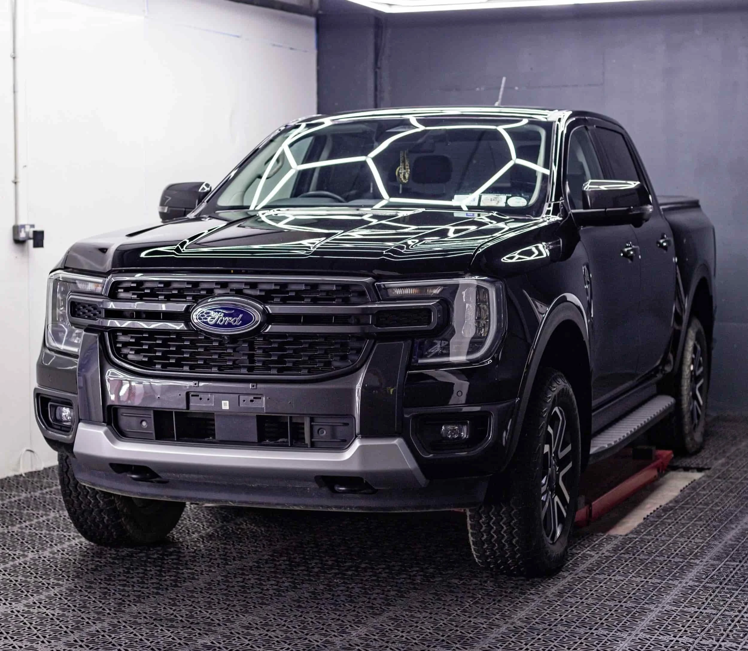 Black Ford pickup truck inside a garage with reflective lighting on the windshield.