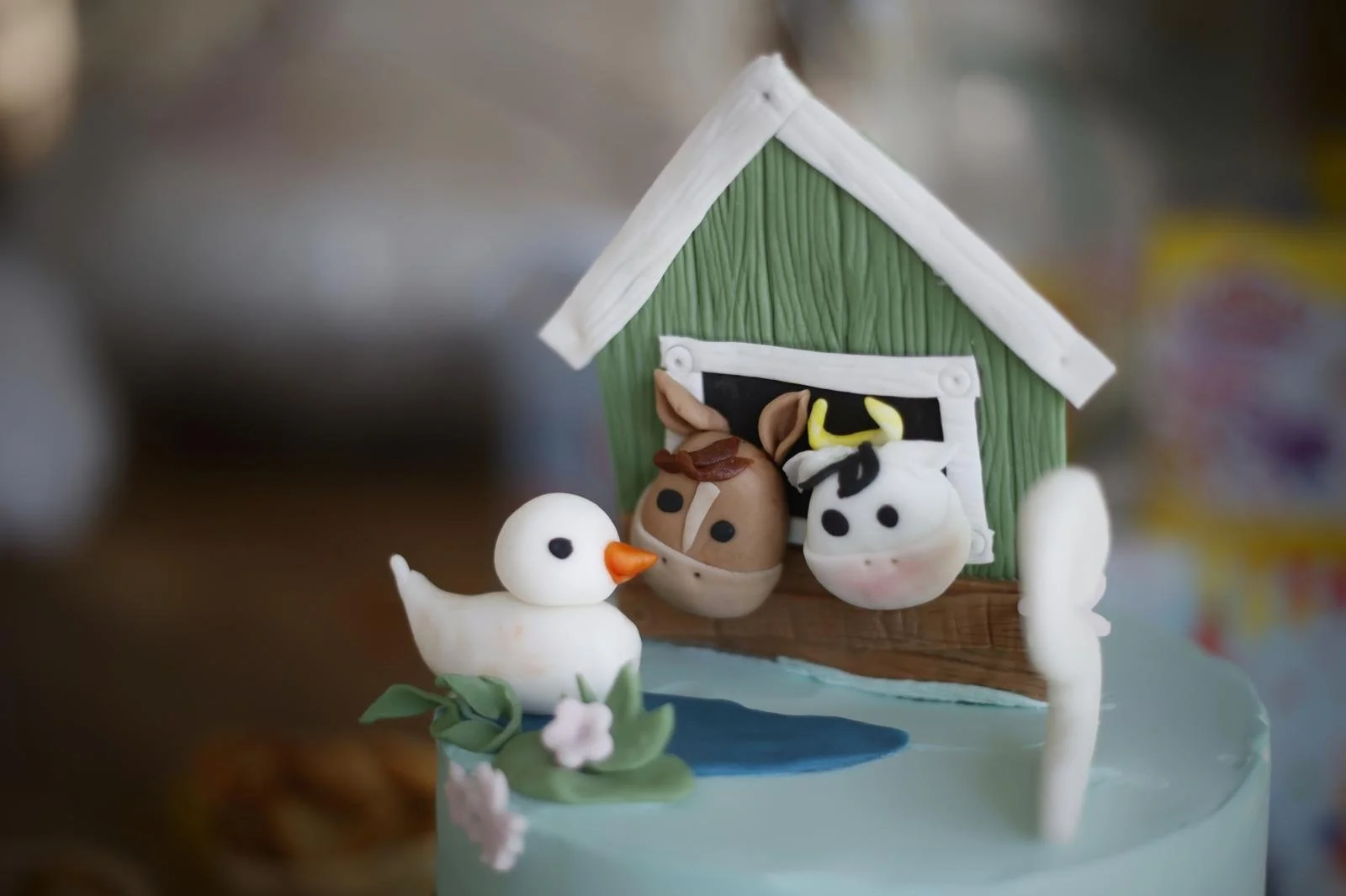 Decoratieve cake met een boerderijthema, met een boerderijhuis, een witte eend, een koe, en een paard, allemaal gemaakt van eetbare materialen.