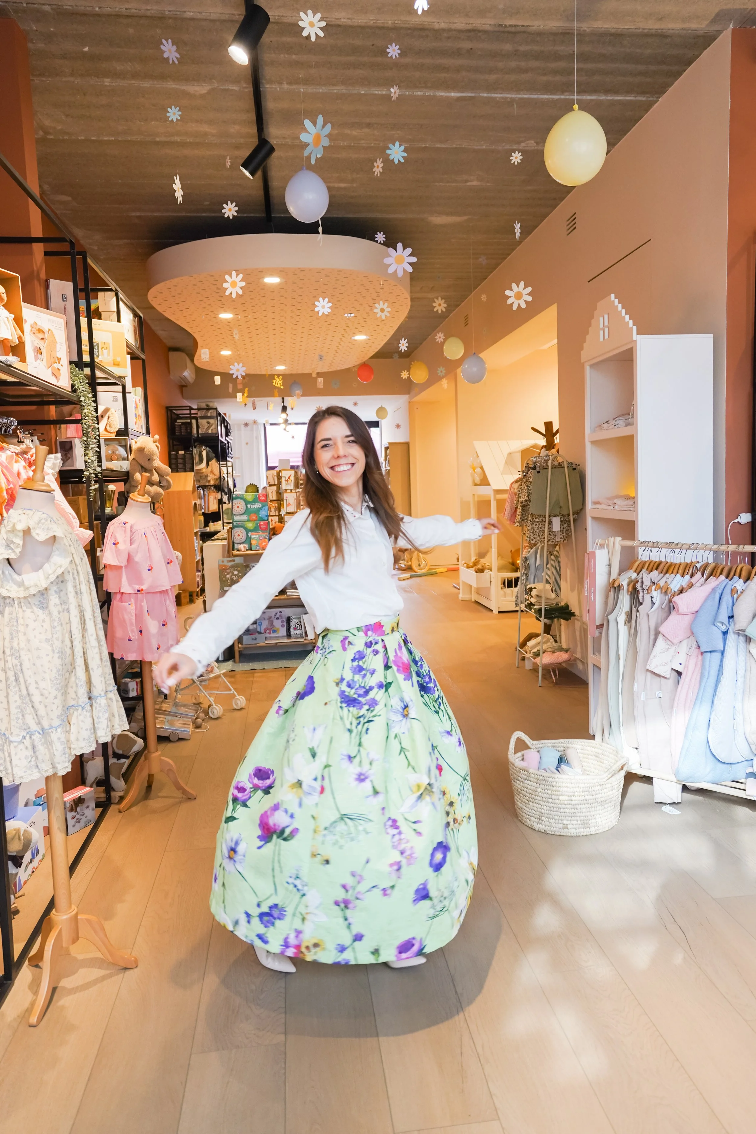 Vrouw draagt een rok met bloemenprint in een boetiek vol kinderkleding en accessoires.