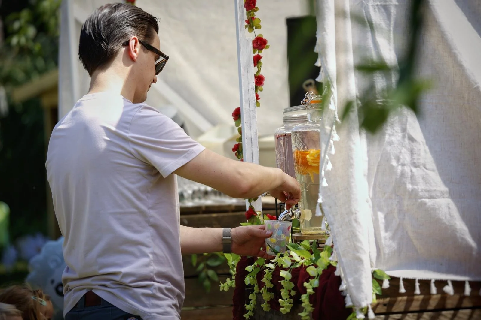Man vult drank uit glazen dispensers met bloemen op een kraam op een markt.