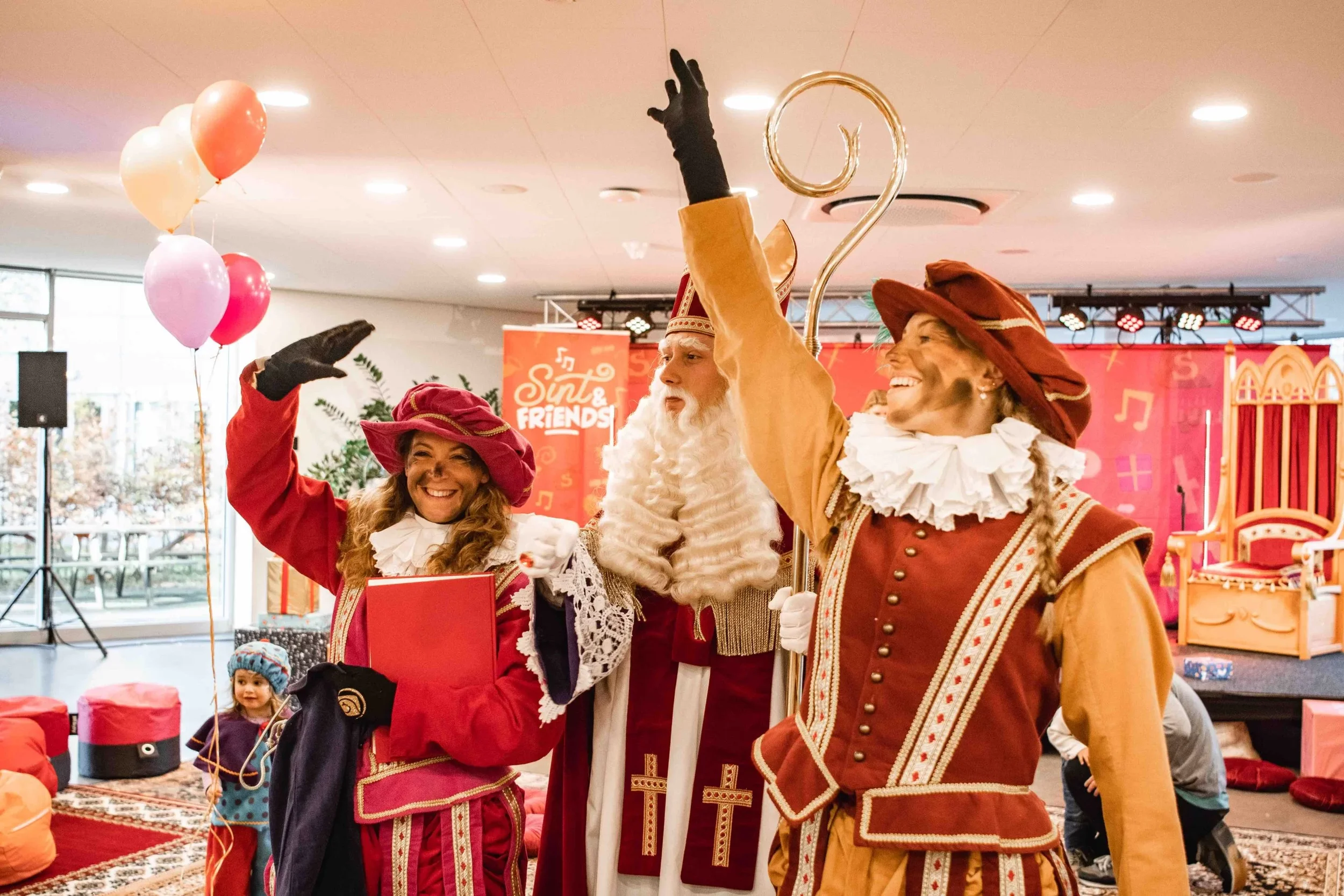 Mensen in Sinterklaas- en Zwarte Piet-kostuums die vieren met ballonnen in een feestzaal.