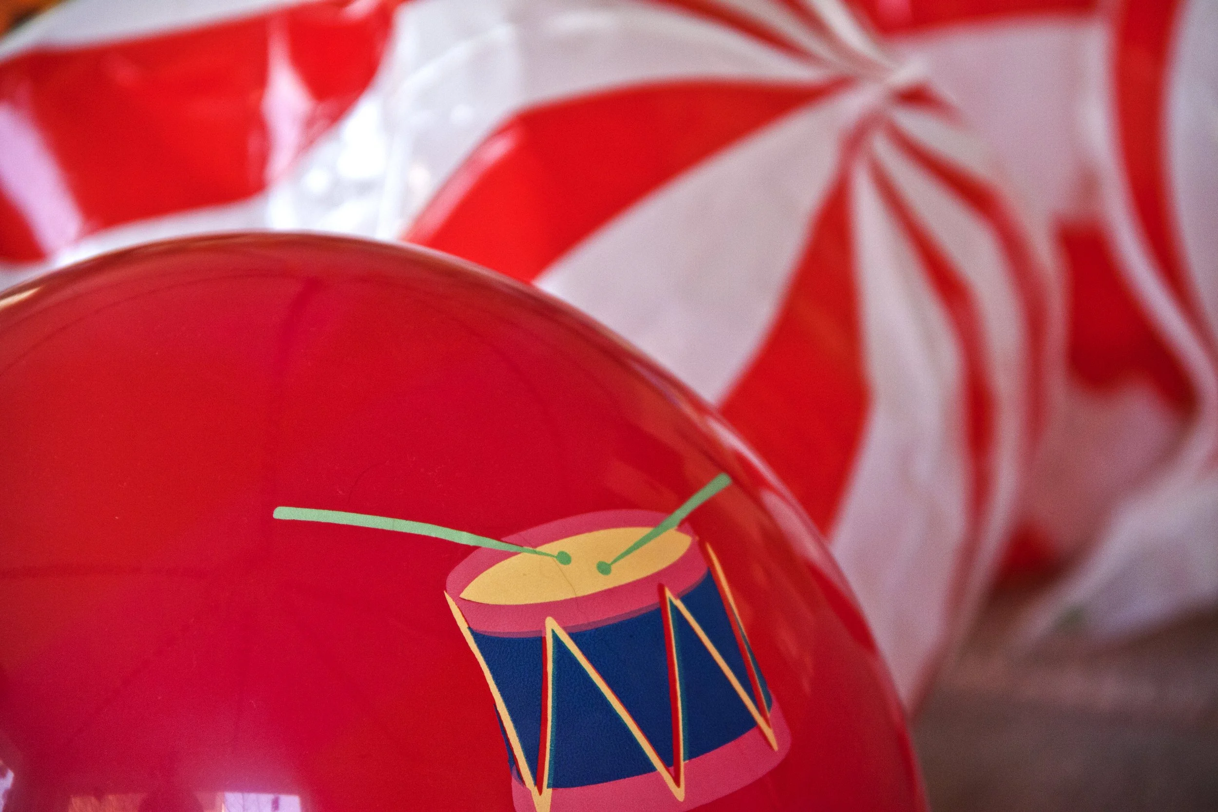 Rode strandbal met trommeltekening en rood-witte strepen op de achtergrond.