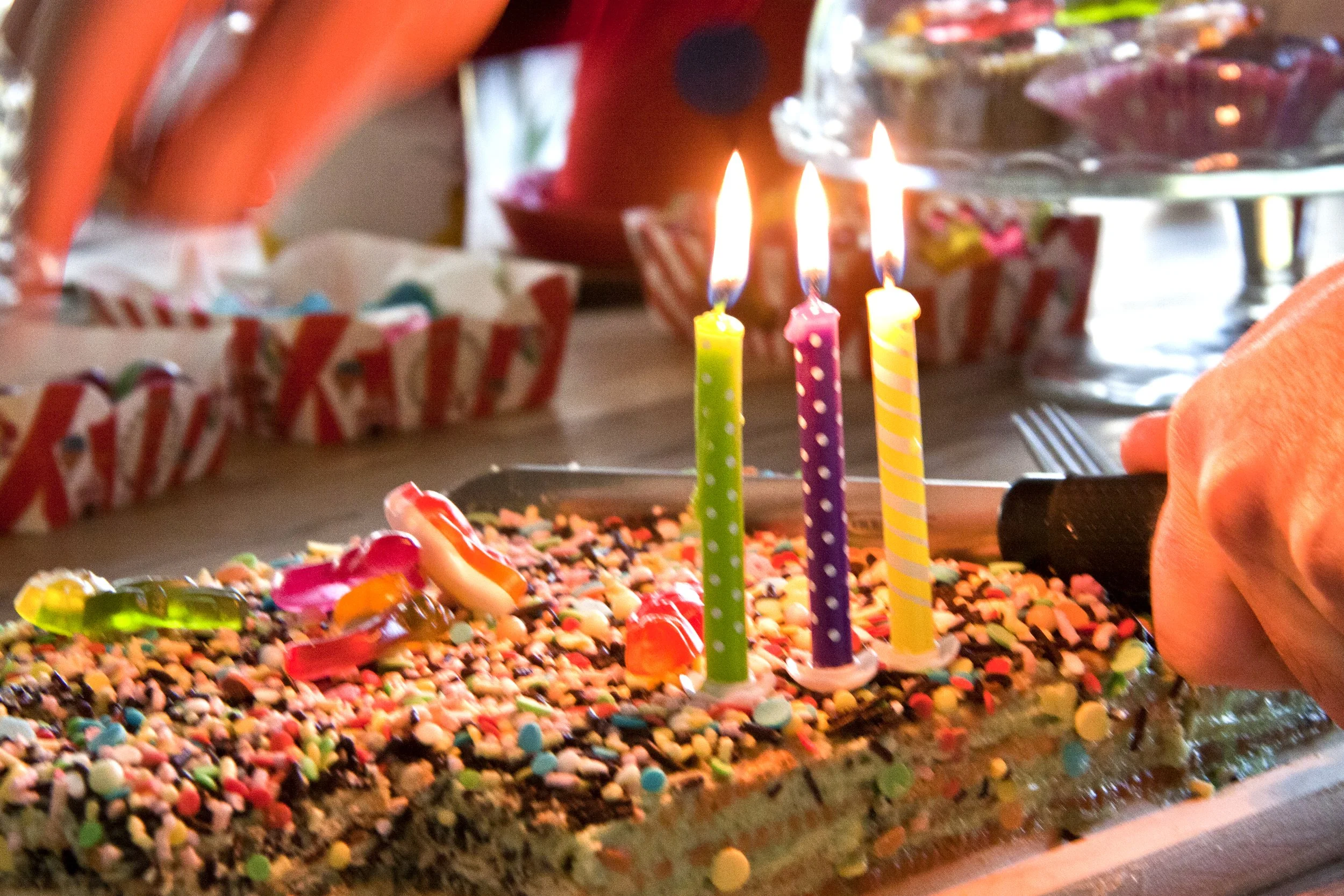 Verjaardagstaart met kleurrijke kaarsen en versieringen, iemand snijdt de taart aan.