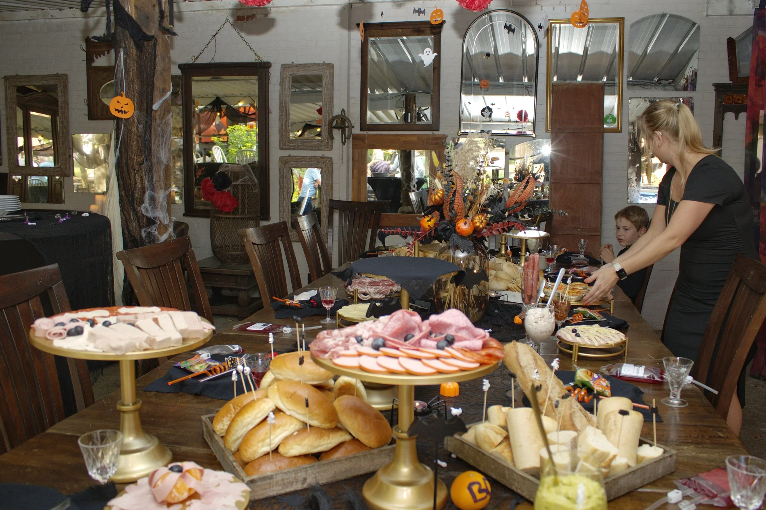 Versierde woonkamer met Halloween-thema, decoraties zoals pompoenen, spinnenwebben en vliegenکی, en een tafel met eten en snacks voor een feest.