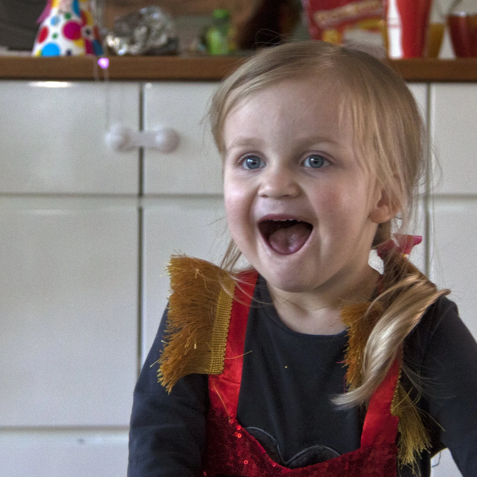 Een jong kind in een feestelijke outfit met pailletten en franjes kijkt opgetogen.