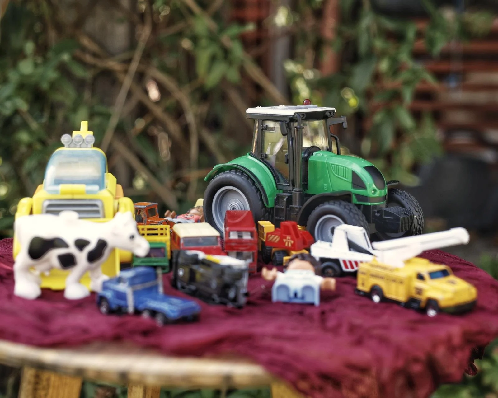 Verschillende speelgoedauto's en tractoren op een rood doek buiten.