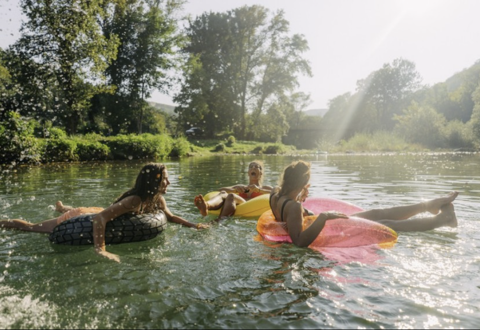San Marcos river float with three women relaxing on floats in a river during a sunny day, surrounded by trees and natural scenery.