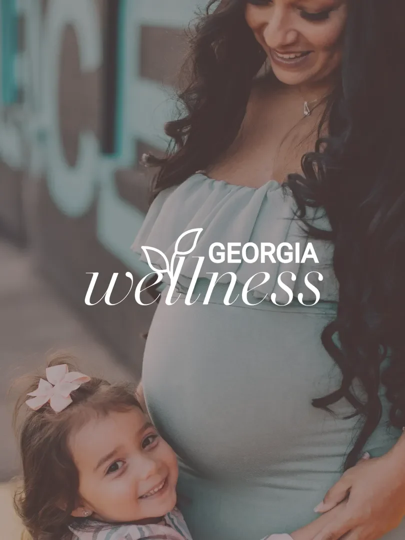A pregnant woman with long dark curly hair smiling and standing outdoors, with a young girl with light brown hair and a pink bow smiling and hugging her. There is a logo overlay for "Obria Medical Clinics"