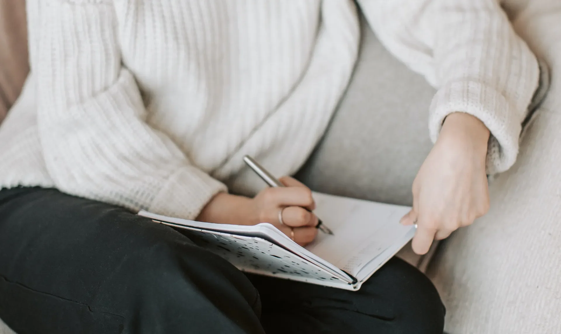Person writing in a notebook while sitting on a sofa.