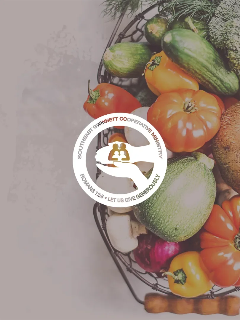 Basket of assorted vegetables including tomatoes, zucchini, bell peppers, onions, and mushrooms with a logo overlay from Southeast Gwinnett Cooperative Ministry.
