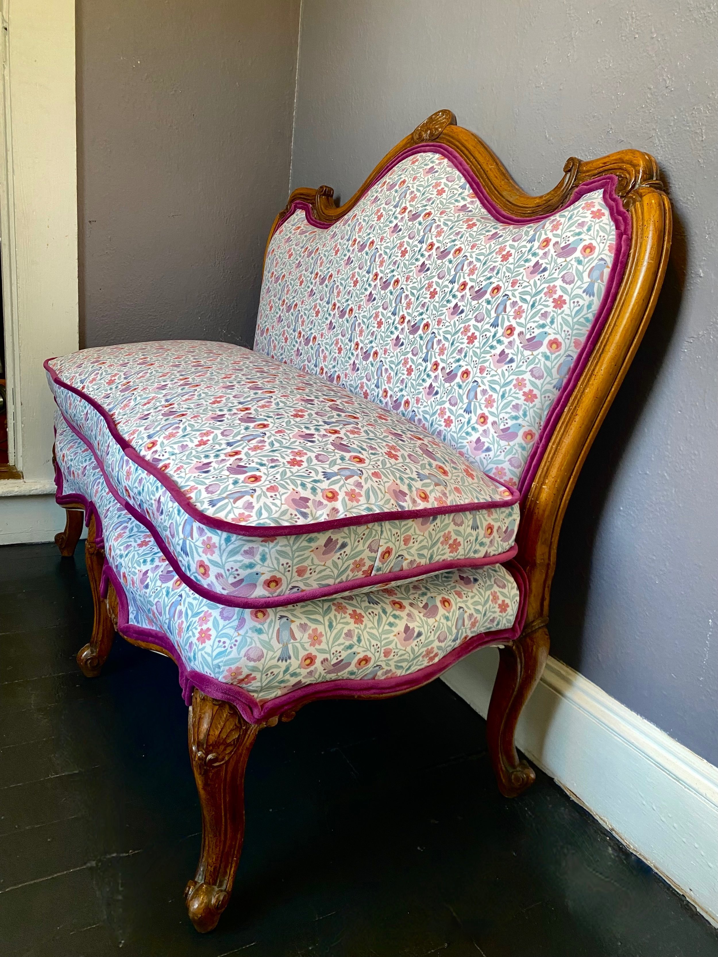Antique wooden settee with eco-conscious recycled canvas floral upholstery and curved legs against a gray wall. Eco-friendly upholstery services. Yarmouth, MA. Cape Cod Upholstery