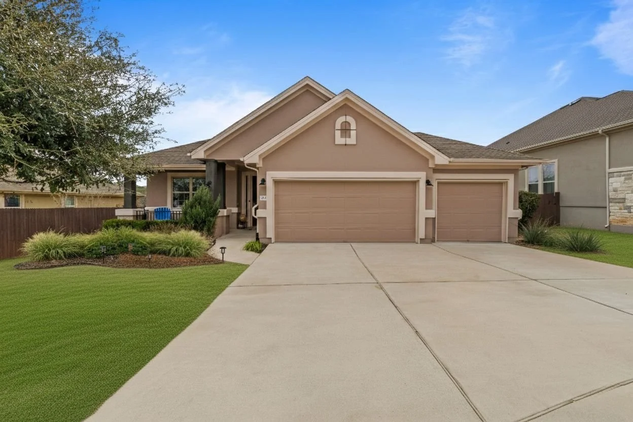 A single-story house with an attached three-car garage, beige exterior, and a front lawn with shrubs and grass, under a partly cloudy sky.