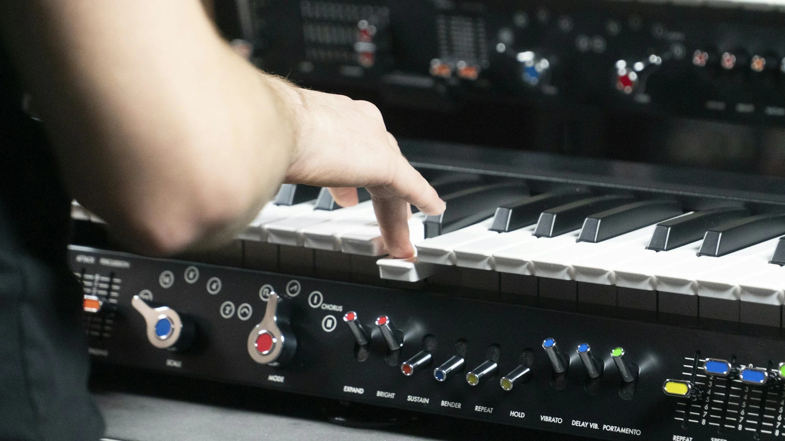 Close-up of a person's hand playing a synthesizer keyboard with various controls and buttons.
