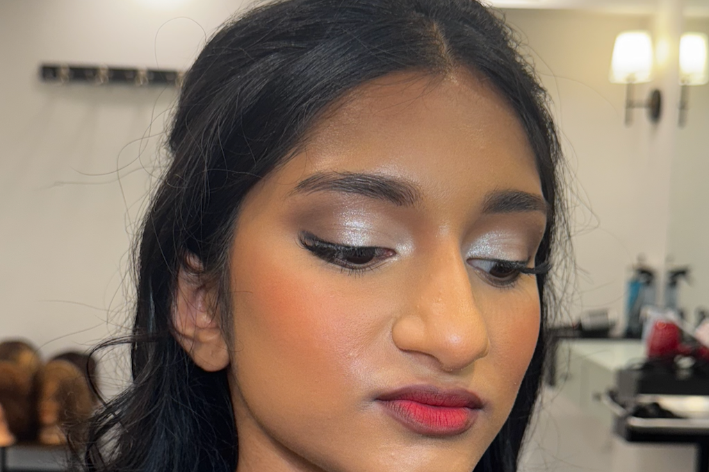Close-up of a woman with dark hair and makeup, including silver eyeshadow, winged eyeliner, and red lipstick, in what appears to be a salon or studio. On-location bridal hair and makeup NJ