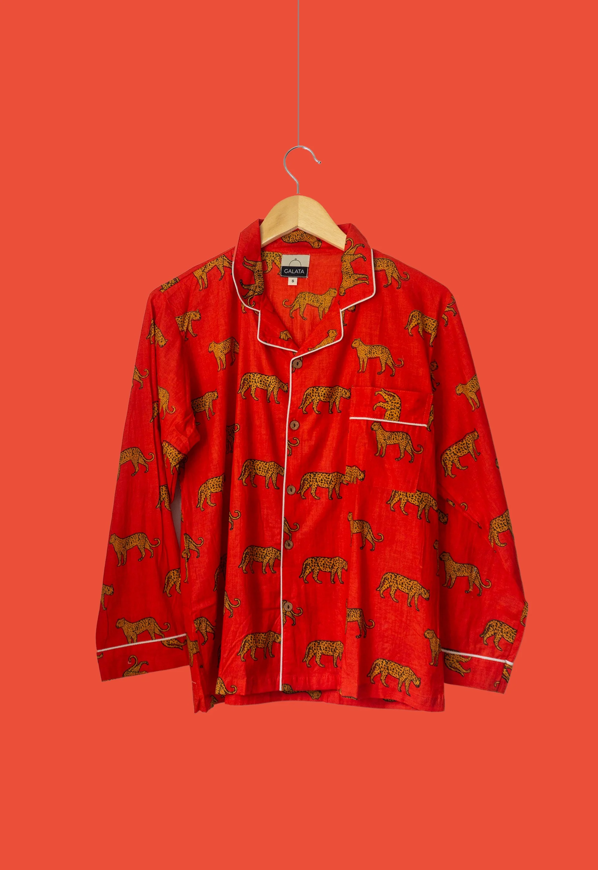 Pijama roja con estampado de leopardos, colgada en una percha sobre un fondo rojo.