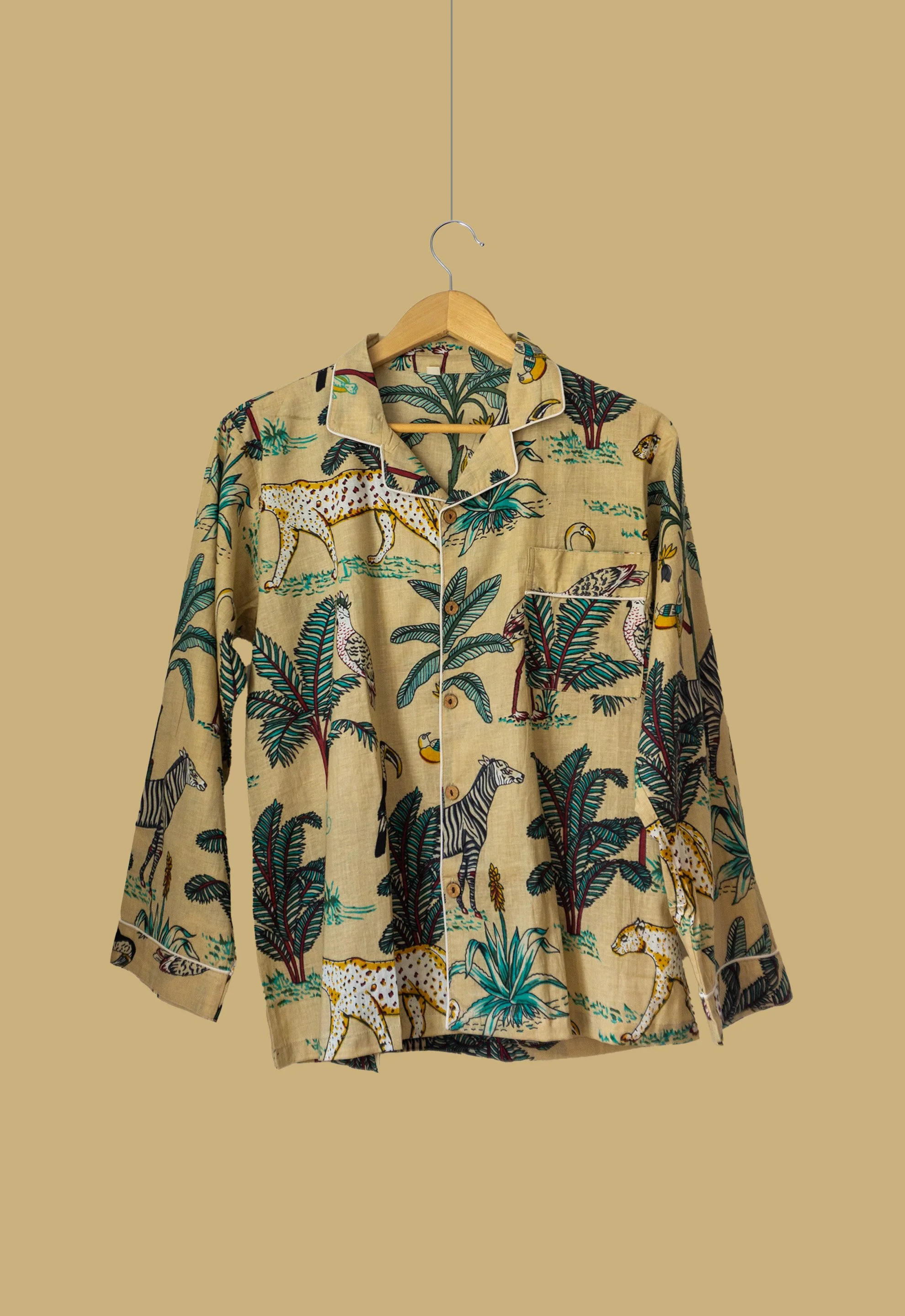 Camisa colgada en una percha con estampado de animales de safari y plantas tropicales sobre un fondo beige.