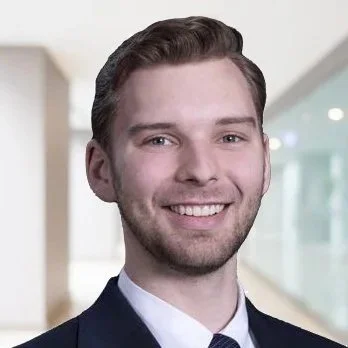A young man in a suit smiling in a modern office setting.