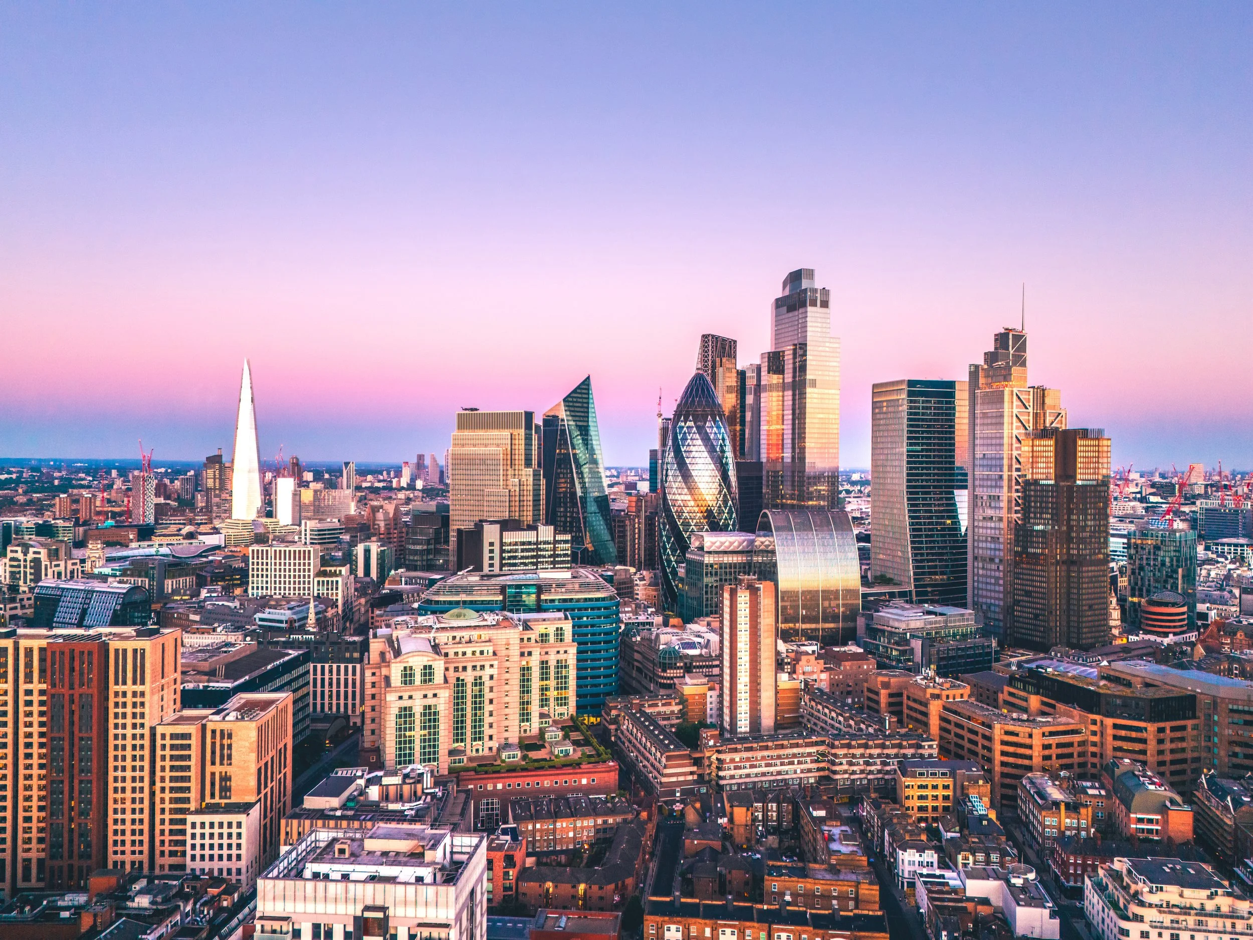 Skyline von London bei Sonnenuntergang mit modernen Wolkenkratzern und pastellfarbenem Himmel.